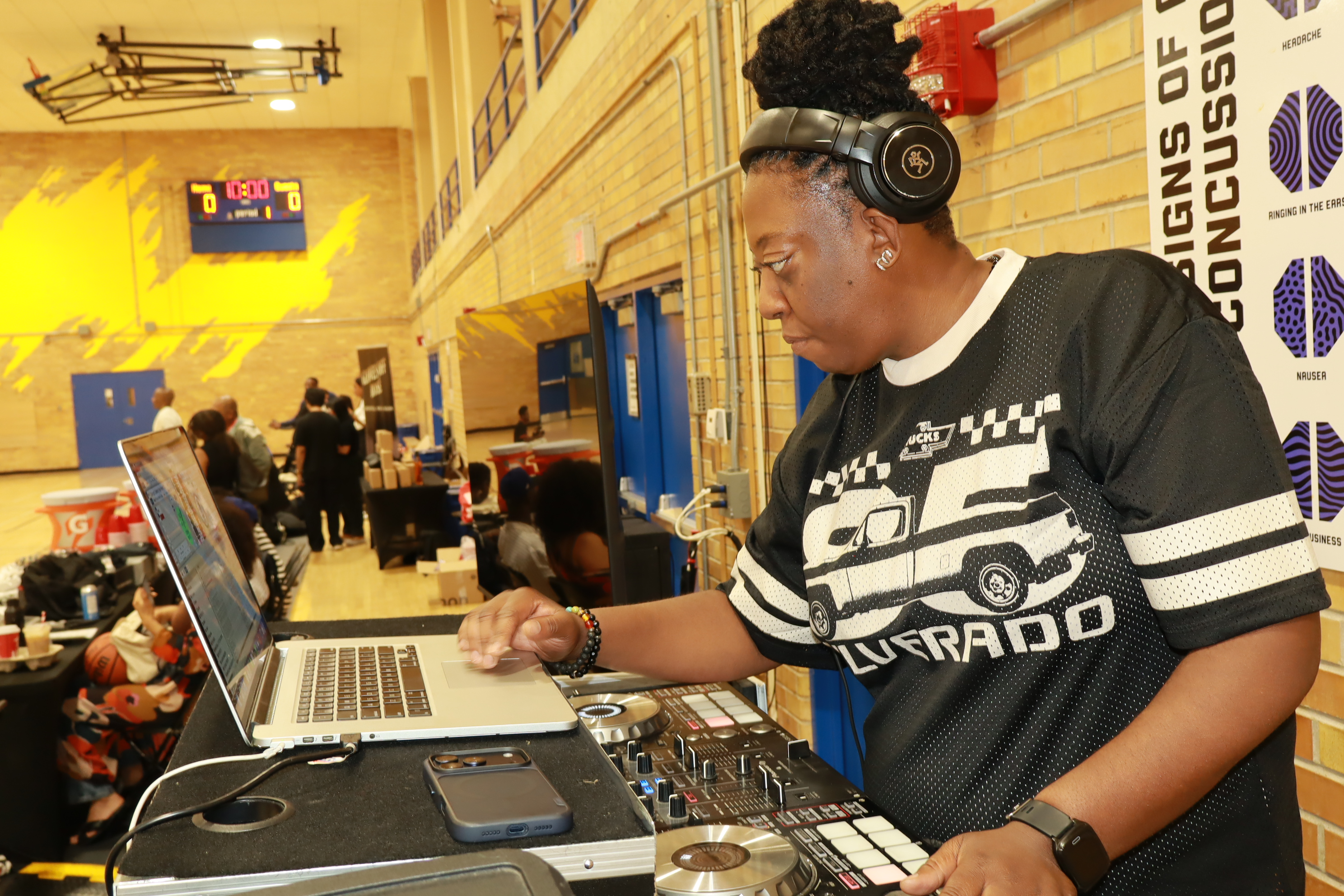 DJ JJ Rock wearing headphones and working at her laptop and DJ controller during a community basketball event