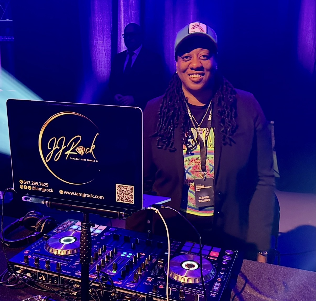 DJ JJ Rock smiling behind her branded laptop and DJ controller at an event