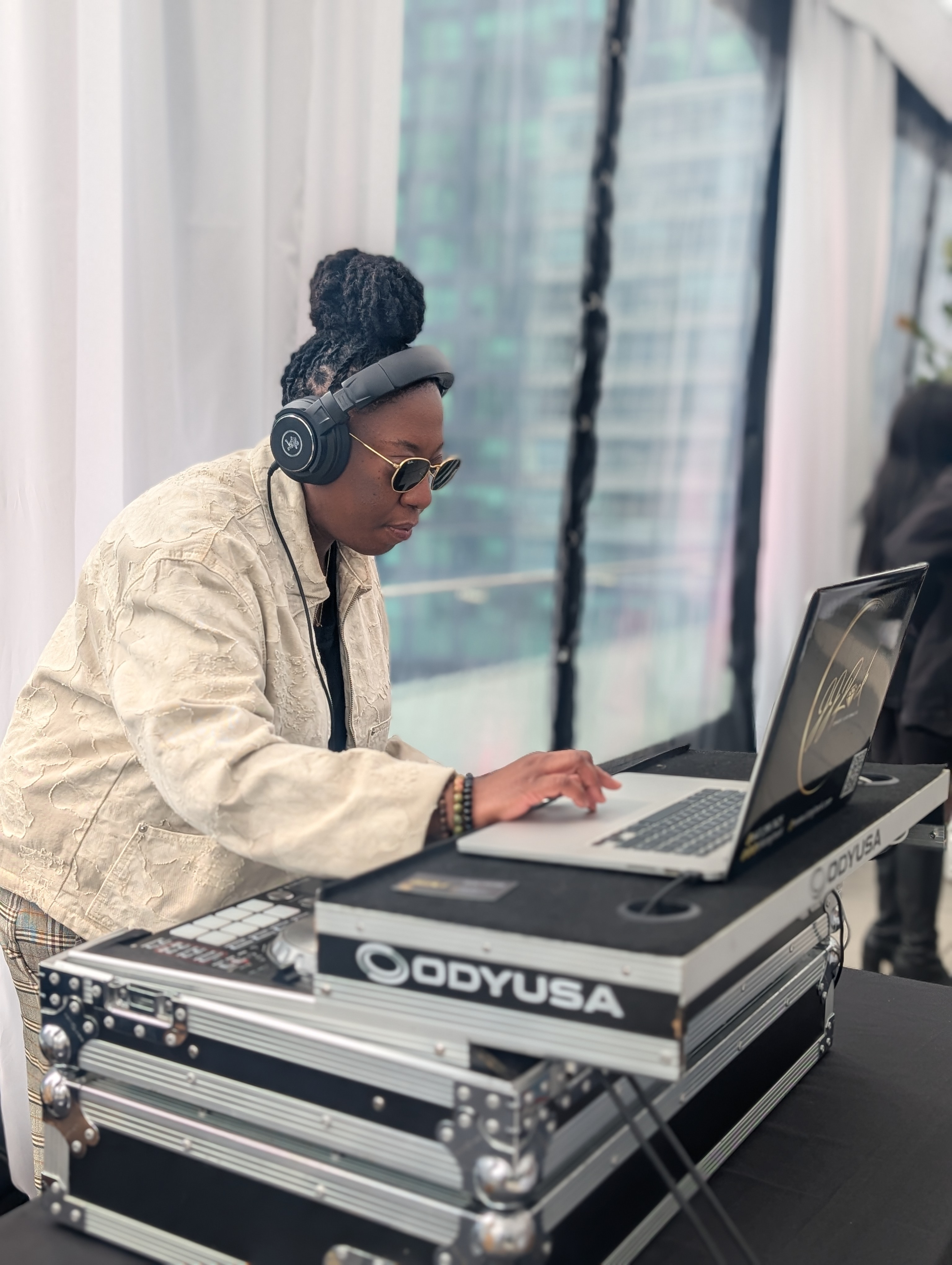 DJ JJ Rock wearing sunglasses and a cream jacket while DJing